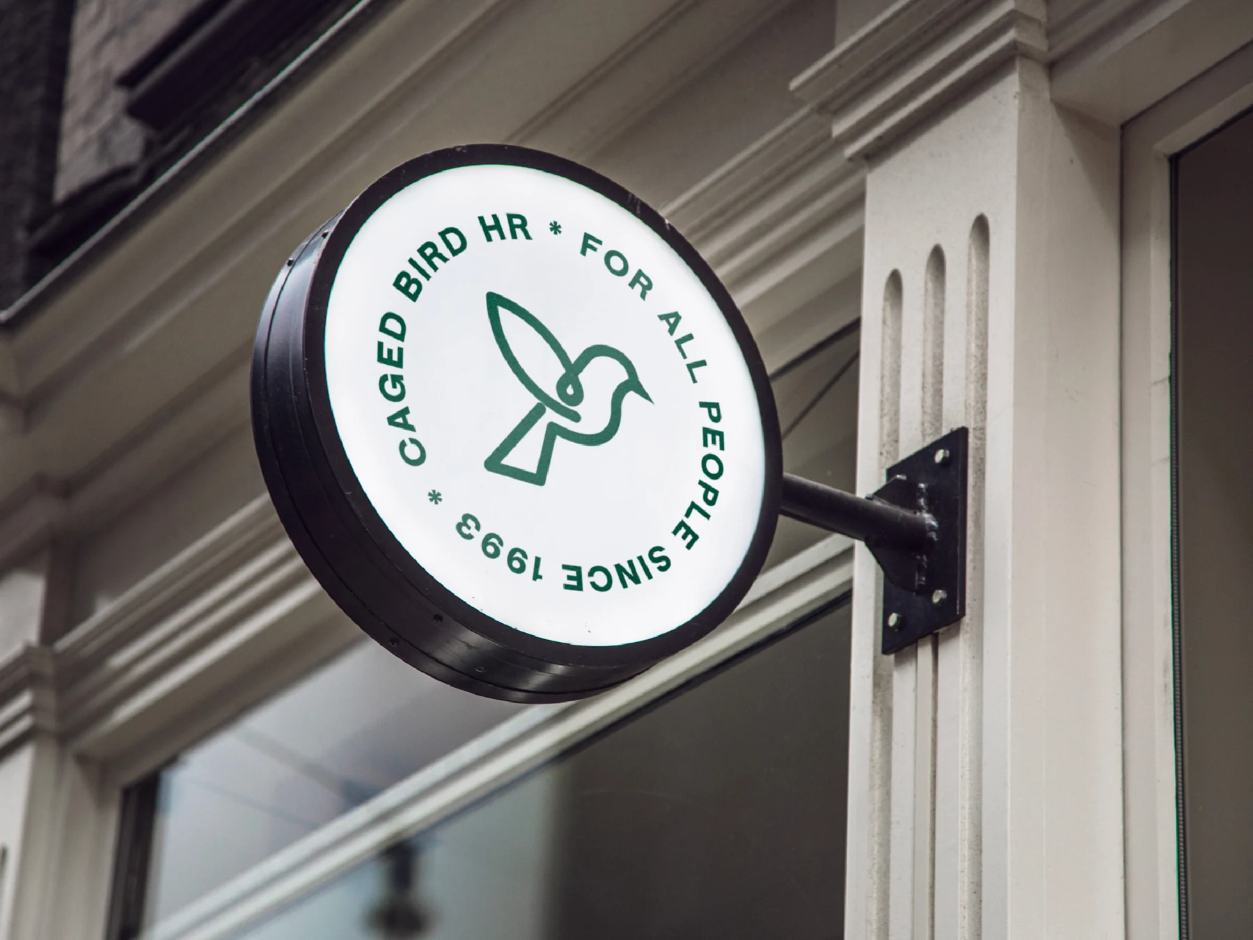 A round Caged Bird HR sign mounted outside a building.
