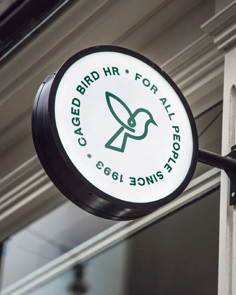 A round Caged Bird HR sign mounted outside a building.