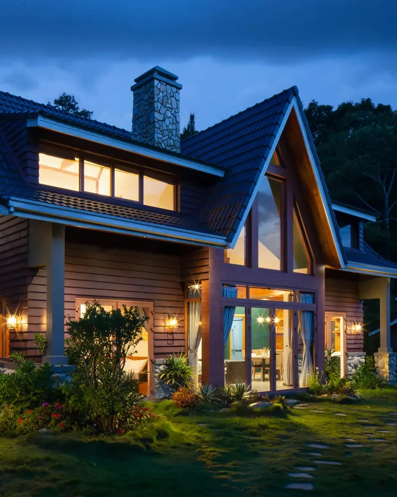 A warmly illuminated A-frame home against a blue twilight sky.