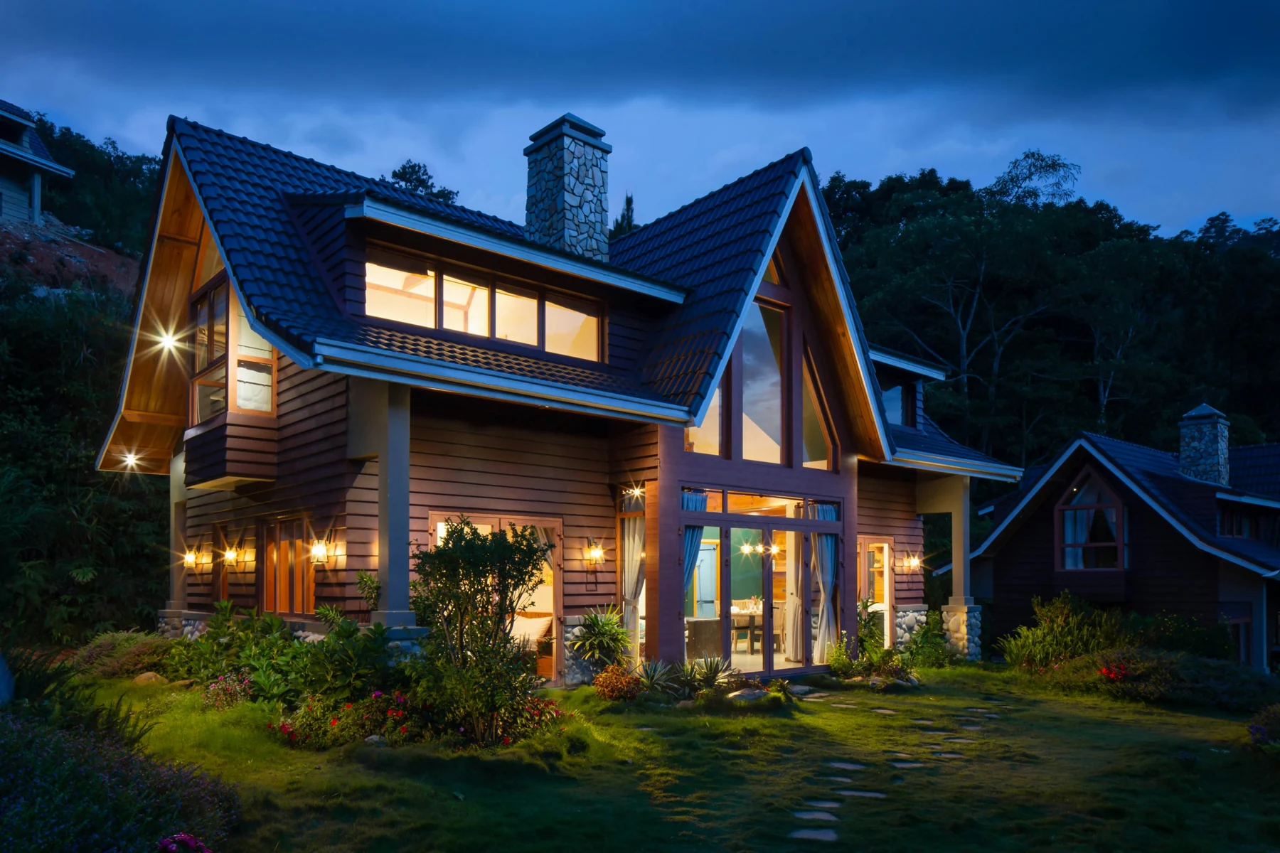 A warmly illuminated A-frame home against a blue twilight sky.